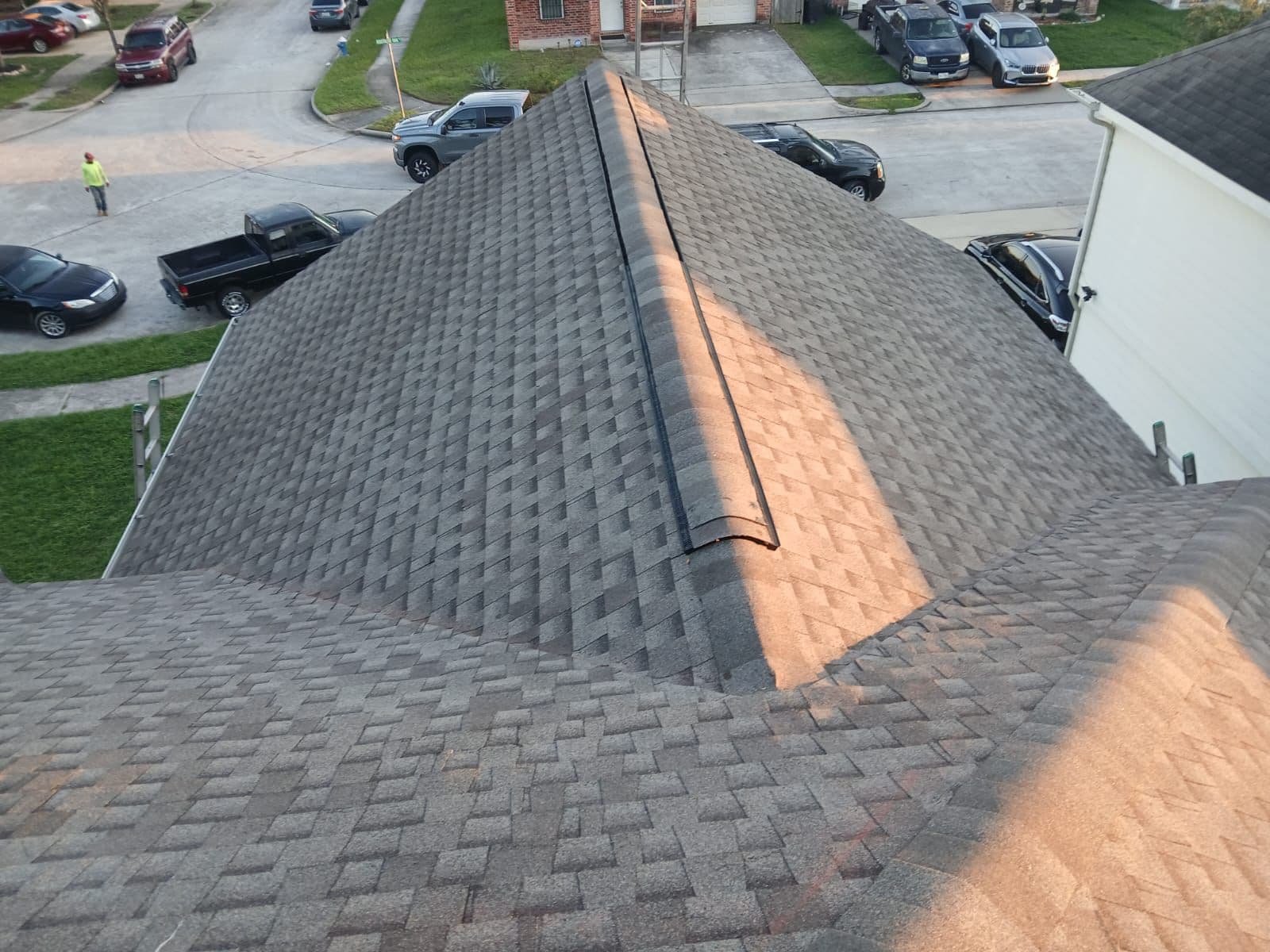 Grey asphalt shingle roof with multiple ridges overlooking a residential street with parked cars.